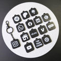Set of black keychains with various app icons on a white circular mat