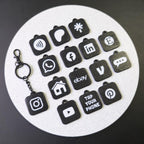 Set of black keychains with various app icons on a white circular mat