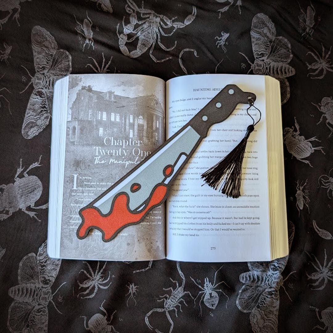 Open book with a knife-shaped bookmark on a dark fabric background