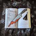 Open book with a knife bookmark and tassel on a dark fabric background with insect illustrations