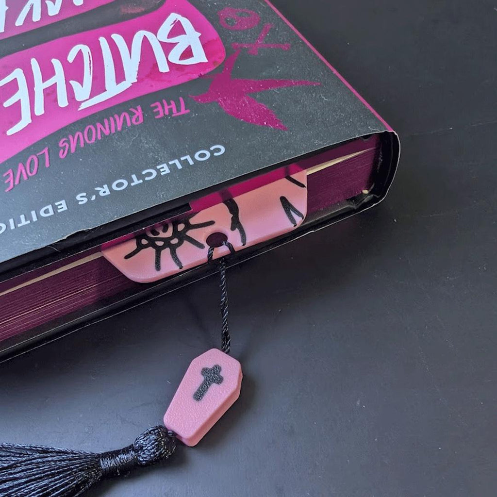 Pink coffin-shaped bookmark with tassel in a book.
