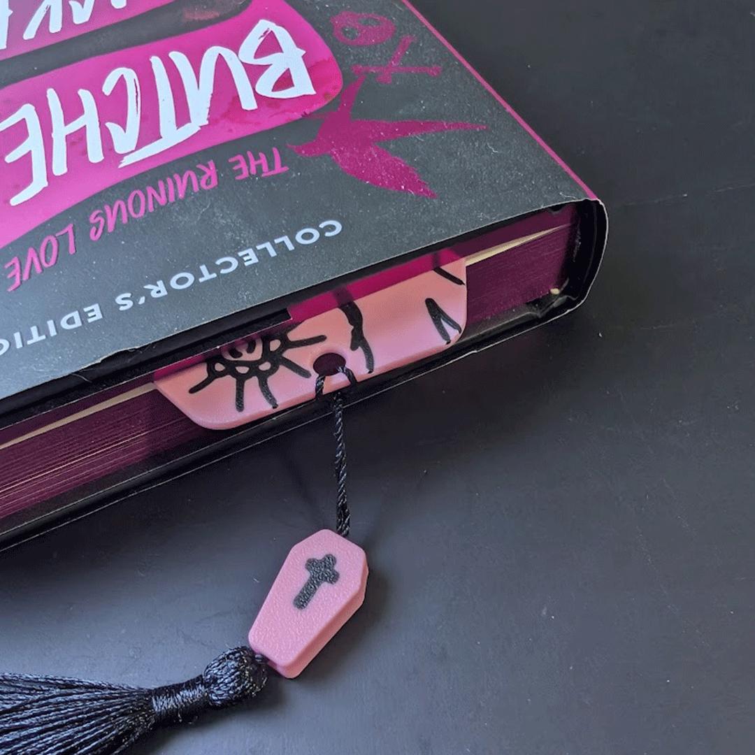 Pink coffin-shaped bookmark with tassel in a book.