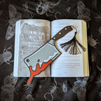 Open book with a bookmark of a cleaver and tassel on a dark fabric background with insect illustrations.